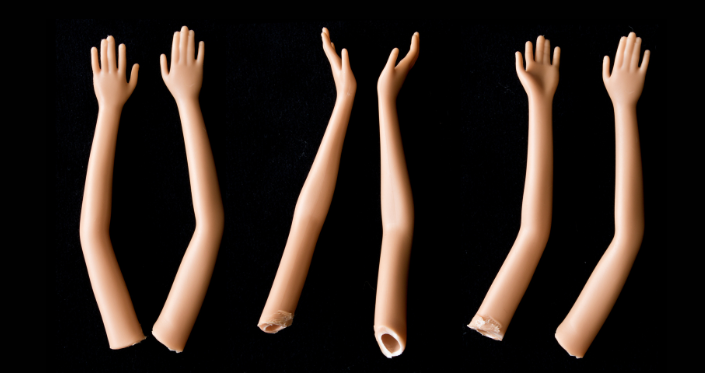 Six arms on a black background, which appear to be torn from Barbie dolls